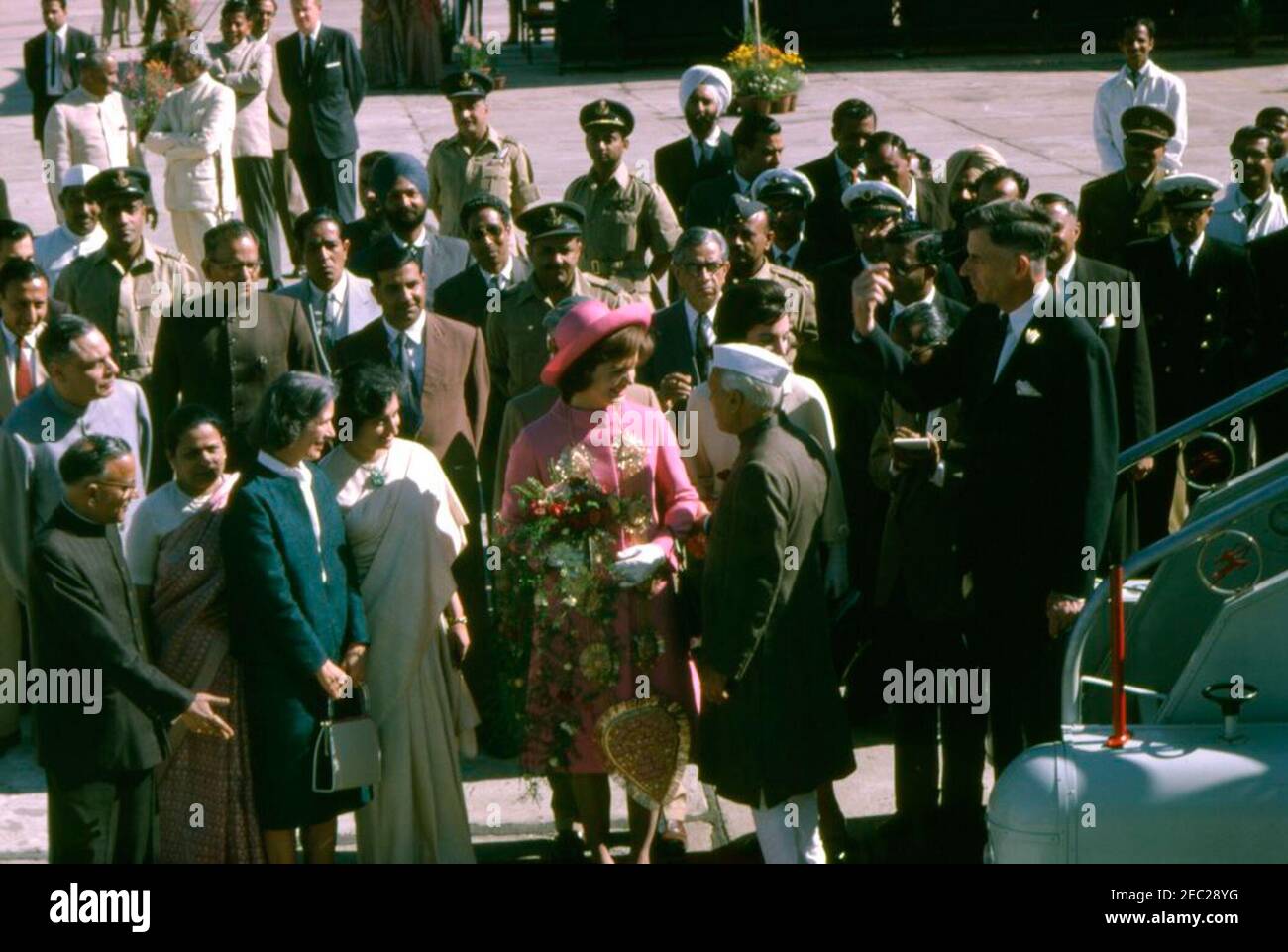 First Lady Jacqueline Kennedyu2019s (JBK) trip to India and Pakistan: New Delhi, Delhi, India, arrival. First Lady Jacqueline Kennedy (center, wearing pink) visits with Prime Minister of India, Jawaharlal Nehru, upon her arrival at Palam Airport in New Delhi, India. Also pictured: Indian Ambassador to the United States, B. K. Nehru (far left, wearing light gray jacket); Kitty Galbraith (front, left), wife of the United States Ambassador to India, John Kenneth Galbraith; daughter of the Prime Minister, Indira Gandhi (left of Mrs. Kennedy); Mrs. Kennedyu2019s sister, Princess Lee Radziwill of Stock Photo