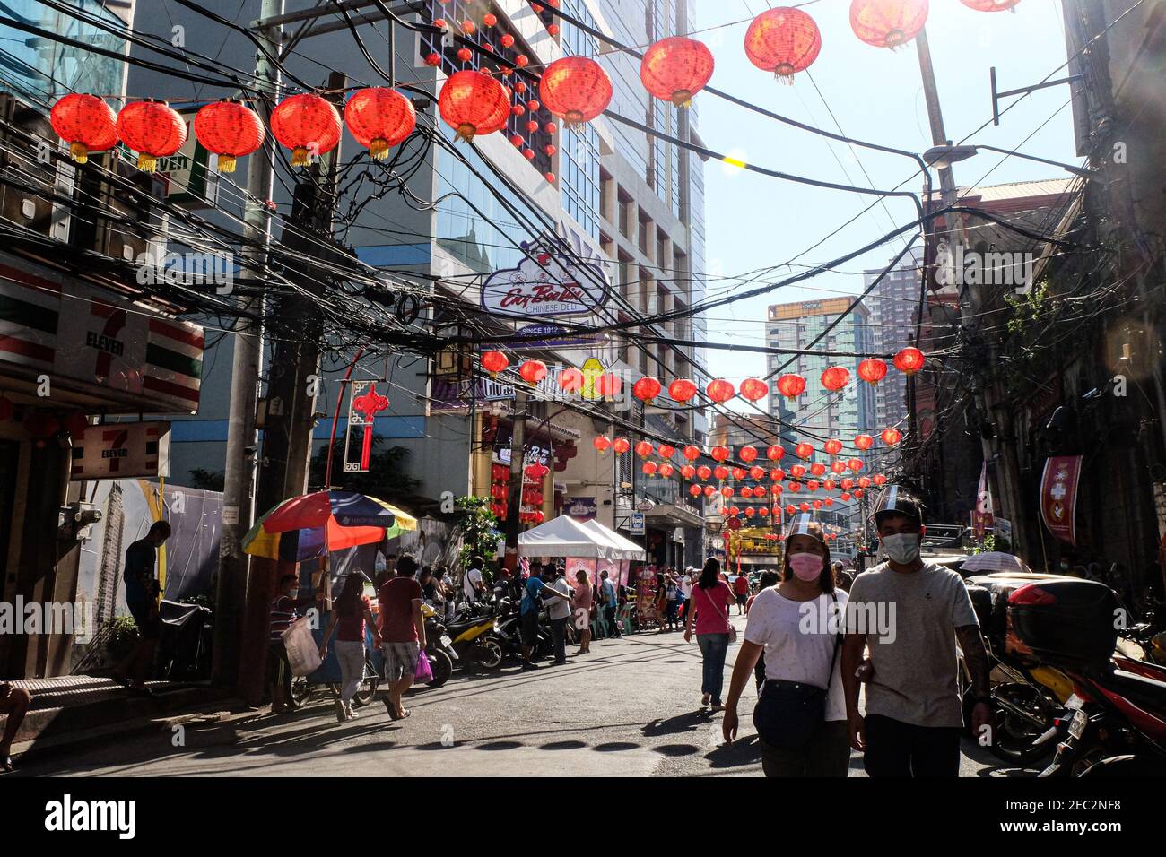 Ongpin St., Binondo, Manila, Philippines. 13th Feb, 2021. People wearing face masks and face shields walk along the streets adorned with Chinese lanterns in Ongpin, Binondo during the celebration of Chinese New Year. Binondo is known as the oldest chinatown in the world, majority of celebrations such as dragon and lion dances were cancelled due to the pandemic. Credit: Majority World CIC/Alamy Live News Stock Photo