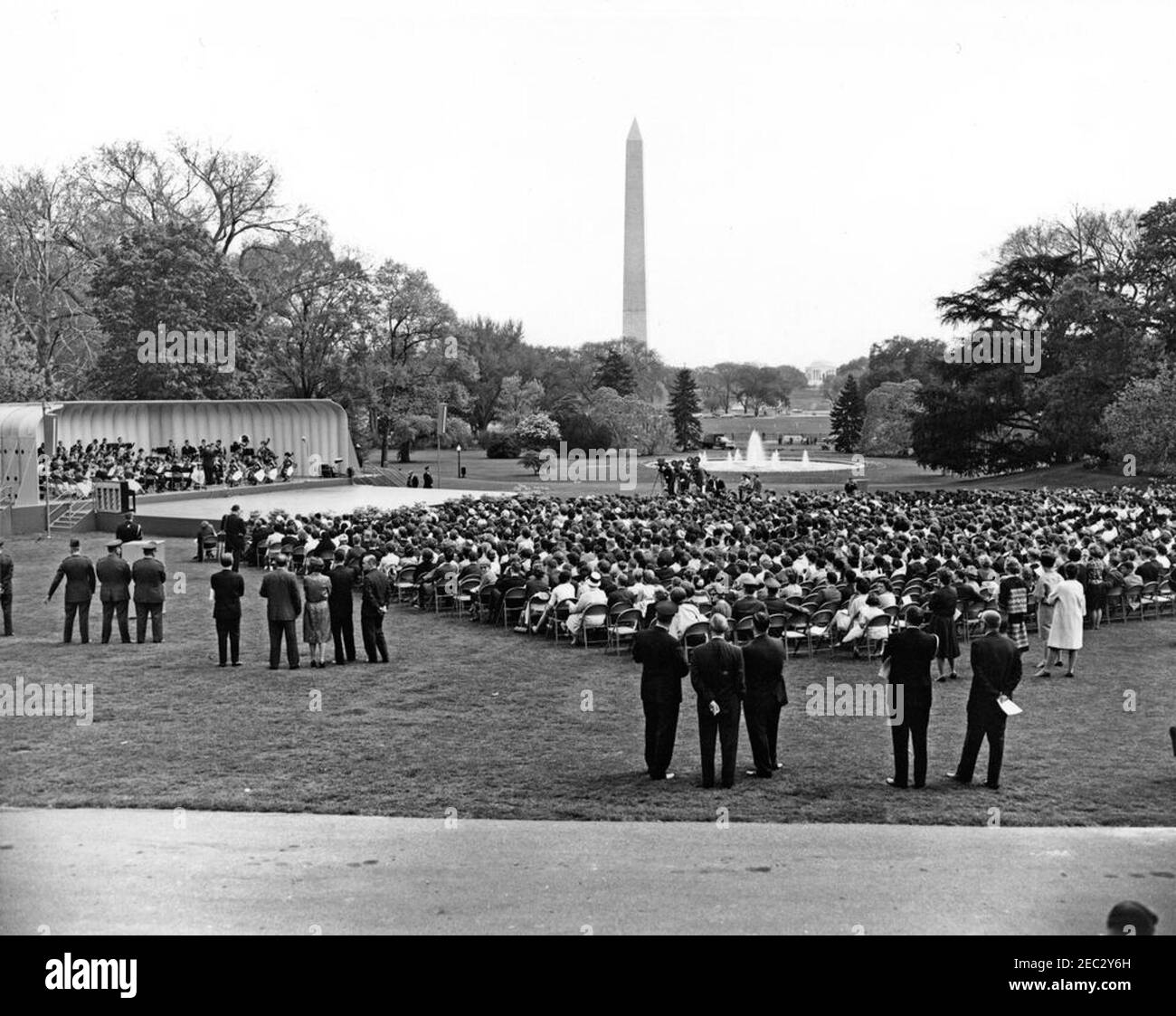 First Lady Jacqueline Kennedyu0027s (JBK) Musical Program for Youth, 2:10PM. An audience assembled on the South Lawn of the White House watches Joseph Pival conduct a performance of the Central Kentucky Youth Symphony Orchestra during the sixth installment of First Lady Jacqueline Kennedyu2019s Musical Programs for Youth by Youth. The Washington Monument and the Jefferson Memorial are visible in the background. Washington, D.C. Stock Photo