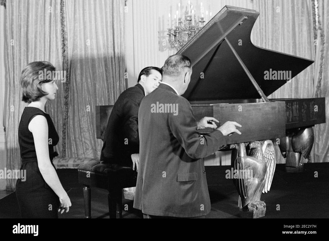 First Lady Jacqueline Kennedyu0027s (JBK) Musical Program for Youth. Korean pianist, Tong-il Han (seated at piano), rehearses in the East Room of the White House, Washington, D.C., prior to performing at the fifth installment of First Lady Jacqueline Kennedyu0027s Musical Programs for Youth by Youth. An unidentified man (back to camera, standing right of Mr. Han) mimes playing the piano; First Ladyu2019s Press Secretary, Pamela Turnure, looks on from left. Mrs. Kennedy held the event for the children of ambassadors, members of Cabinet, and State Department officials living in Washington, D. Stock Photo