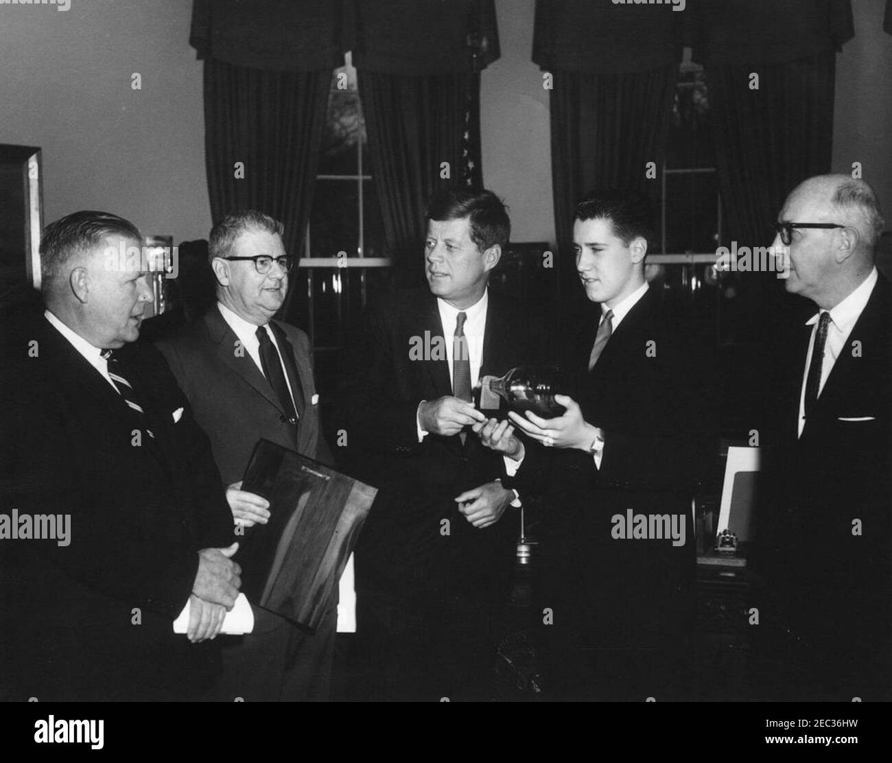 Visit of the Boysu0027 Clubsu0027 u0022Boy of the Year,u0022 Stephen Lutz, 10:57AM. President John F. Kennedy (center) holds a scale model, enclosed inside a bottle, of PT Boat 109, presented to him by the Boysu0027 Clubs of Americau0027s (BCA) u0022Boy of the Yearu0022 Stephen Lutz of Newark, New Jersey. (L-R) Albert L. Cole, President of the BCA; John M. Gleason, National Director of the BCA; President Kennedy; Stephen Lutz; and Charles R. Messier, Executive Director of the Boysu0027 Clubs of Newark, New Jersey. Oval Office, White House, Washington, D.C. Stock Photo