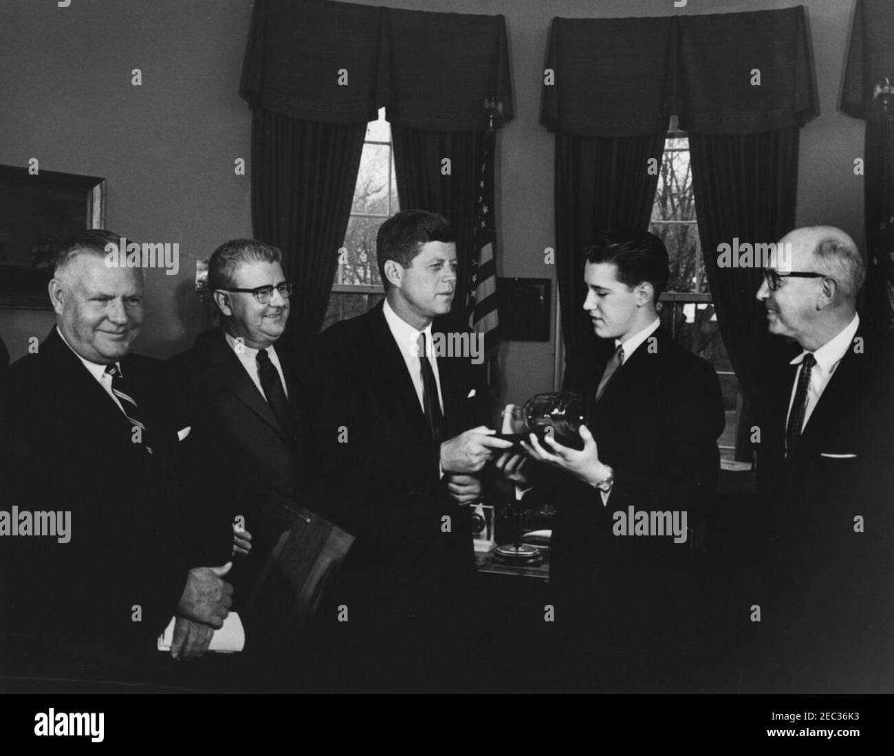 Visit of the Boysu0027 Clubsu0027 u0022Boy of the Year,u0022 Stephen Lutz, 10:57AM. President John F. Kennedy (center) holds a scale model, enclosed inside a bottle, of PT Boat 109, presented to him by the Boysu0027 Clubs of Americau0027s (BCA) u0022Boy of the Yearu0022 Stephen Lutz of Newark, New Jersey. (L-R) Albert L. Cole, President of the BCA; John M. Gleason, National Director of the BCA; President Kennedy; Stephen Lutz; and Charles R. Messier, Executive Director of the Boysu0027 Clubs of Newark, New Jersey. Oval Office, White House, Washington, D.C. Stock Photo