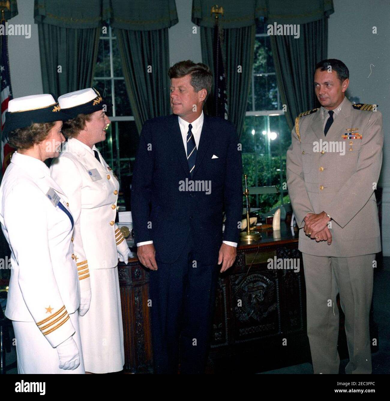Visit of Captain Winifred Quick Collins, Director of Women Accepted for Volunteer Emergency Service (WAVES), 9:48AM. President John F. Kennedy visits with U.S. Navy officers. Left to right: Women Accepted for Volunteer Emergency Service (WAVES) officer, Commander Irene Wolensky; Director of WAVES, Captain Winifred Quick Collins; President Kennedy; and Naval Aide to the President, Captain Tazewell T. Shepard, Jr. Oval Office, White House, Washington, D.C. Stock Photo