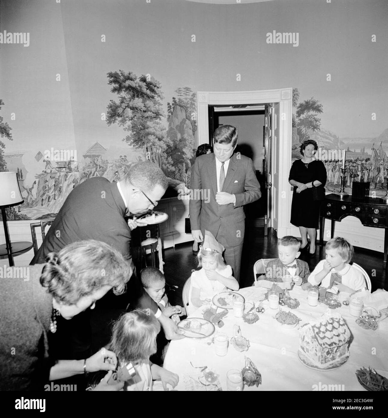 Birthday party for Caroline Kennedy and John F. Kennedy, Jr.. President John F. Kennedy stands behind his daughter, Caroline Kennedy, during a joint birthday party for Caroline and John F. Kennedy, Jr.; White House butler, Robert B. Thompson, Jr. (left), serves food to Avery Hatcher, son of Associate Press Secretary, Andrew T. Hatcher (seated left of Caroline). Presidentu2019s Dining Room (Residence), White House, Washington, D.C. Stock Photo