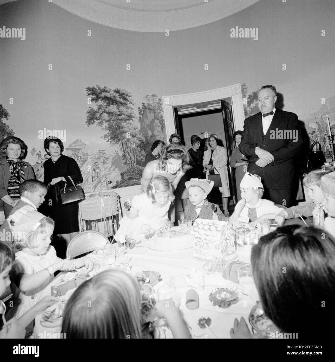 Birthday party for Caroline Kennedy and John F. Kennedy, Jr.. Caroline Kennedy blows out the candles on her cake during a joint birthday party for her and her brother, John F. Kennedy, Jr.; First Lady Jacqueline Kennedy stands behind her daughter. Also pictured: Avery Hatcher, son of Associate Press Secretary, Andrew T. Hatcher; White House butler, John W. Ficklin. Presidentu2019s Dining Room (Residence), White House, Washington, D.C. Stock Photo