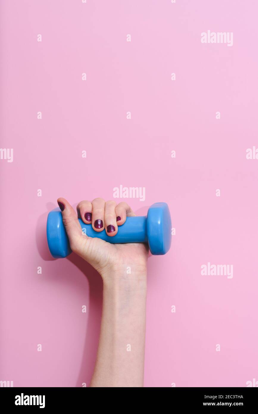 vertical studio take of the hand of a caucasian woman with violet polish on nails holding blue dumb bell on a pink background Stock Photo