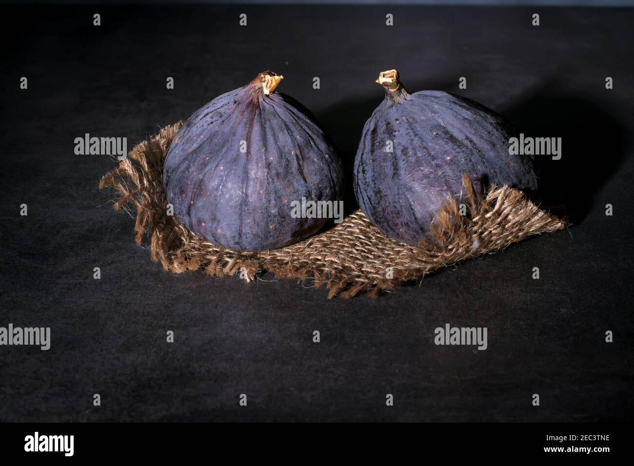 Two ripe purple figs lie on coarse cloth and on a concrete top. Stock Photo