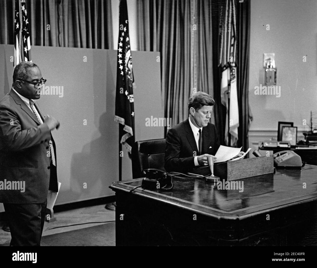 Radio u0026 Television Address to the Nation regarding desegregation at the University of Alabama, 8:00PM. President John F. Kennedy prepares to deliver a radio and television address to the nation regarding desegregation at the University of Alabama. Associate Press Secretary, Andrew T. Hatcher, stands at left. Oval Office, White House, Washington, D.C. Stock Photo