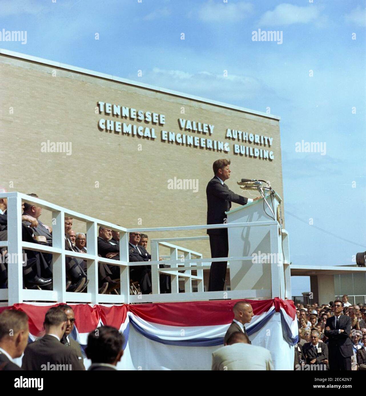 Trip to Tennessee and Alabama: Arrival at Muscle Shoals, Alabama, and Address at the 30th Anniversary celebration of the Tennessee Valley Authority (TVA). President John F. Kennedy (right, at lectern) delivers an address from the speakersu0027 platform in front of the Tennessee Valley Authorityu0027s (TVA) Chemical Engineering Building at a celebration commemorating the 30th anniversary of the TVA. Those seated on the platform include: Senator Lister Hill (Alabama); Governor of Alabama George C. Wallace; Frank E. Smith, member of the TVA Board; Aubrey J. u201cRedu201d Wagner, Chairman of t Stock Photo