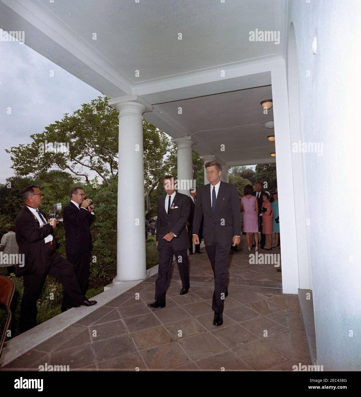 Presentation of the National Aeronautics and Space Administration (NASA) Distinguished Service Medal (DSM) to Astronaut Major L. Gordon Cooper, 12:15PM. President John F. Kennedy and astronaut Major L. Gordon Cooper walk along the West Wing Colonnade, following Major Cooperu2019s National Aeronautics and Space Administration (NASA) Distinguished Service Medal (DSM) presentation ceremony. Standing at right in background: First Lady Jacqueline Kennedy; Vice President Lyndon B. Johnson; Major Cooperu2019s daughters, Janita and Camala. Two unidentified photographers stand at left. White House, W Stock Photo