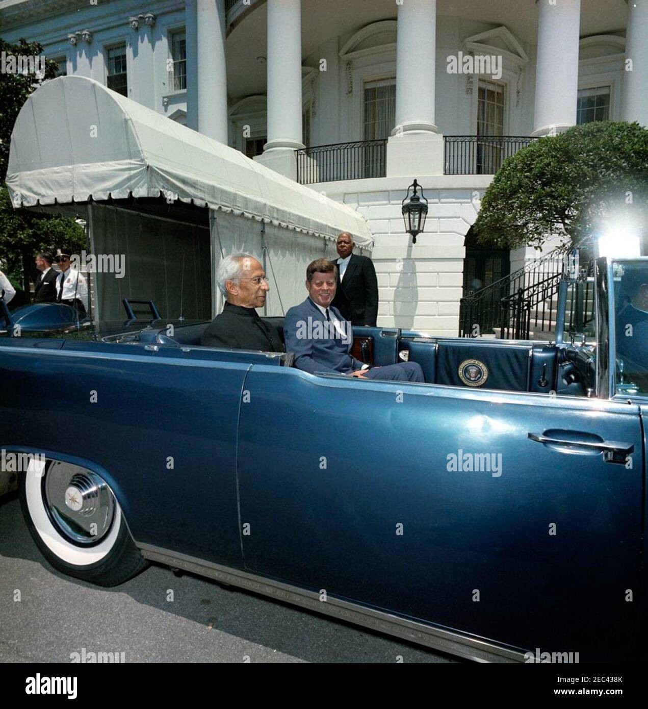 Parade in honor of Dr. Sarvepalli Radhakrishnan, President of India, 12:35PM. President John F. Kennedy and President of India, Dr. Sarvepalli Radhakrishnan, sit in the back seat of the presidential limousine (Lincoln-Mercury Continental convertible) prior to a parade in honor of President Radhakrishnan. Special Assistant to President Kennedy, John J. McNally (head turned), stands at far left in background. South Lawn driveway, White House, Washington, D.C. Stock Photo
