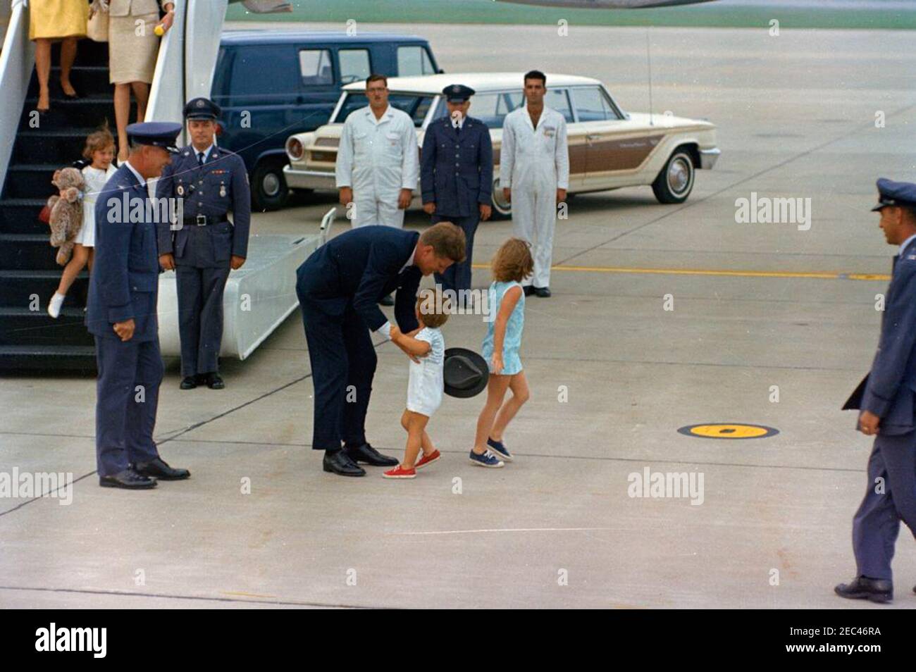 Weekend at Hyannis Port: President Kennedy with Caroline Kennedy (CBK) and John F. Kennedy, Jr. (JFK Jr.), at Otis Air Force Base. President John F. Kennedy (at left, holding hat) greets his son, John F. Kennedy, Jr., upon his arrival at Otis Air Force Base, Cape Cod, Massachusetts. Caroline Kennedy (facing away from camera) stands to the right of President Kennedy and John, Jr; United States Air Force Lieutenant Thomas O. Johnson stands at center of group in front of car in the background. All others are unidentified. Stock Photo