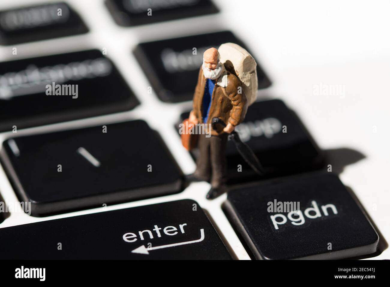 Tiny old traveler on white notebook keyboard with black buttons. Internet browsing or programming. Elder man computer education concept. Notebook keyb Stock Photo