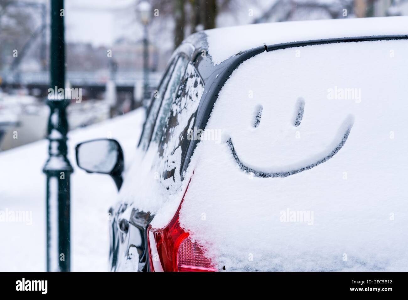 Parked car covered in snow at wintertime with a smiley face emoji drawn on the rear window of the automobile on the street. Stock Photo
