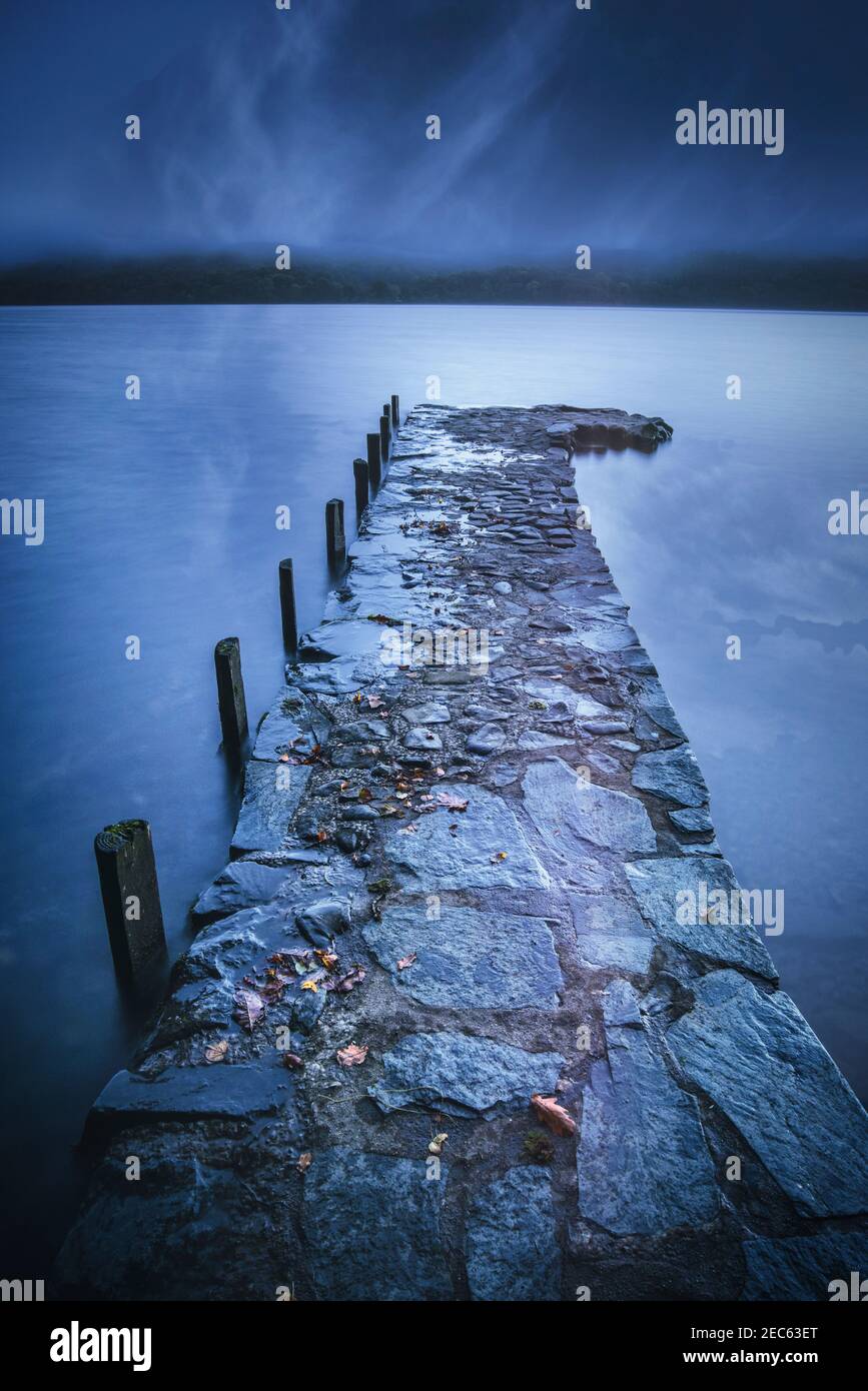 Stone built jetty stretching out into the still waters of Coniston Water, Lake District National Park, Cumbria, UK Stock Photo