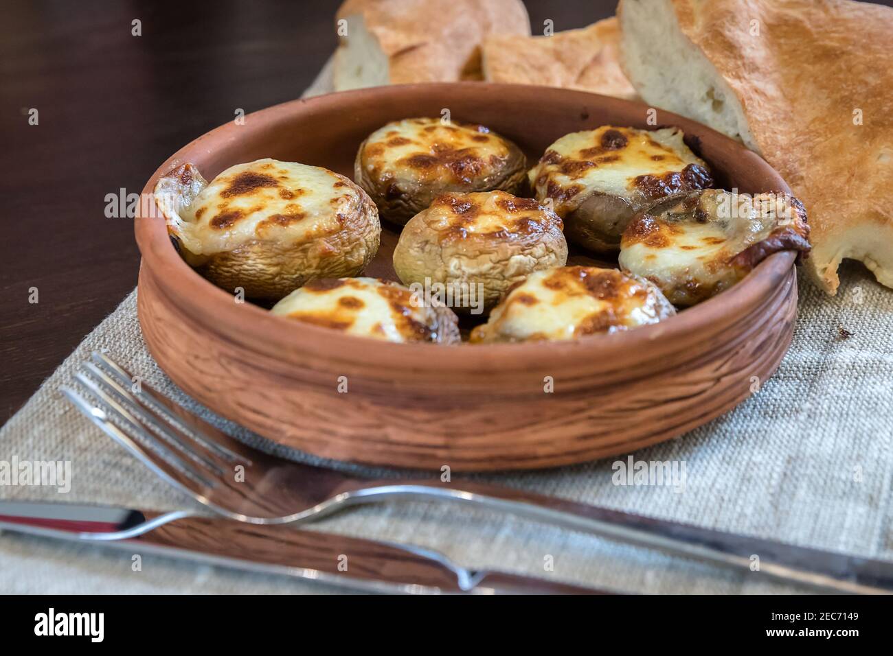 Mushrooms, Sulguni Cheese in Clay Pots, pita and cutlery close up on the table. Georgian traditional food. Stock Photo