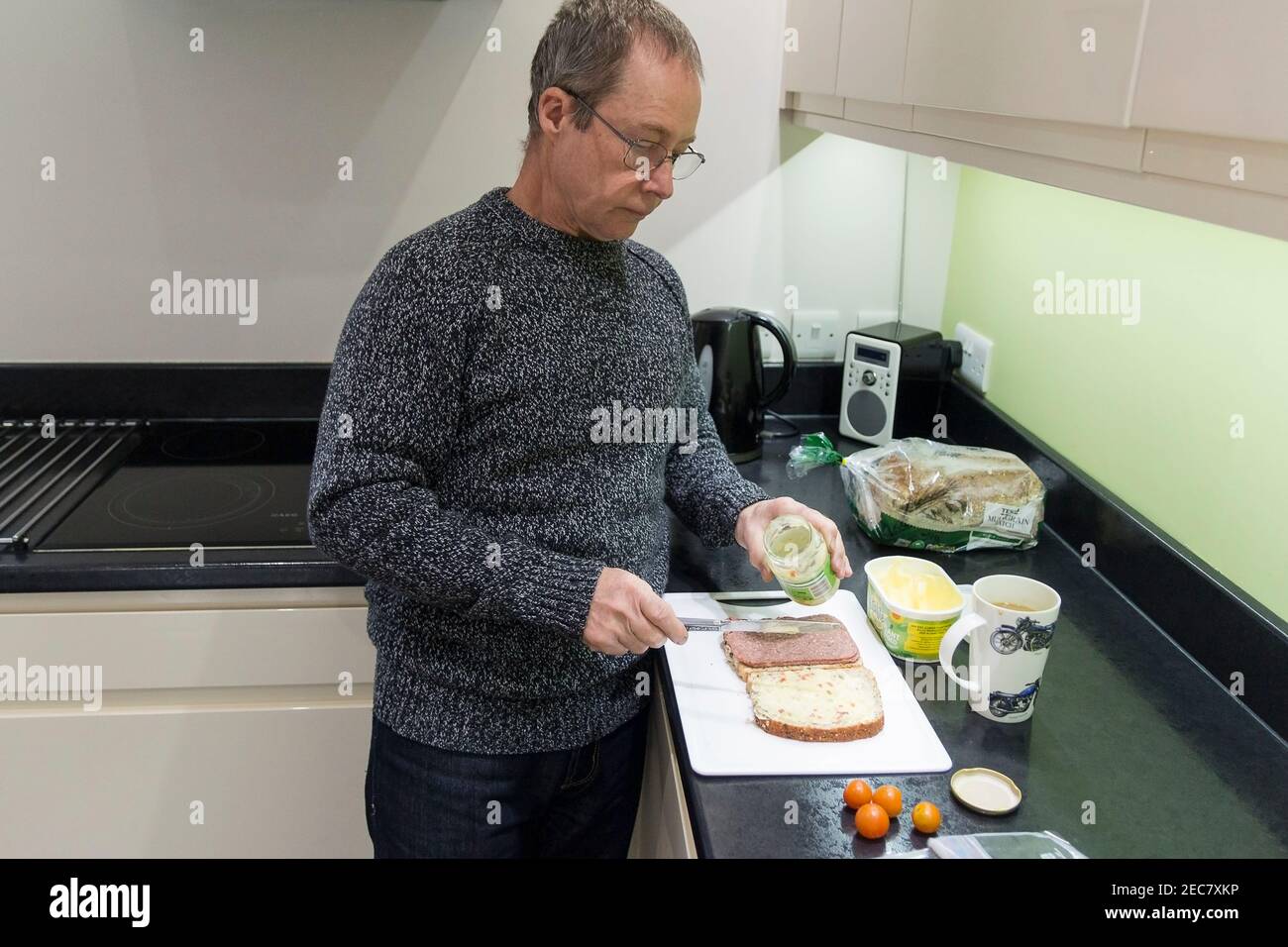 Sandwich making pensioner male making a corned beef and tomato sandwich at home in the kitchen during lock down 2020. One self image of seven taken. Stock Photo
