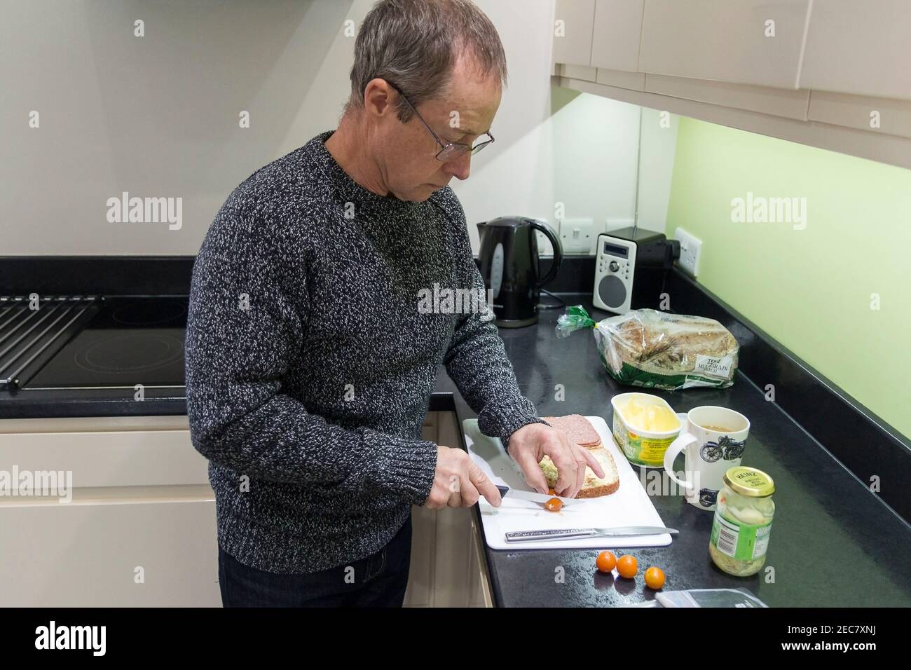 Sandwich making pensioner male making a corned beef and tomato sandwich at home in the kitchen during lock down 2020. One self image of seven taken. Stock Photo