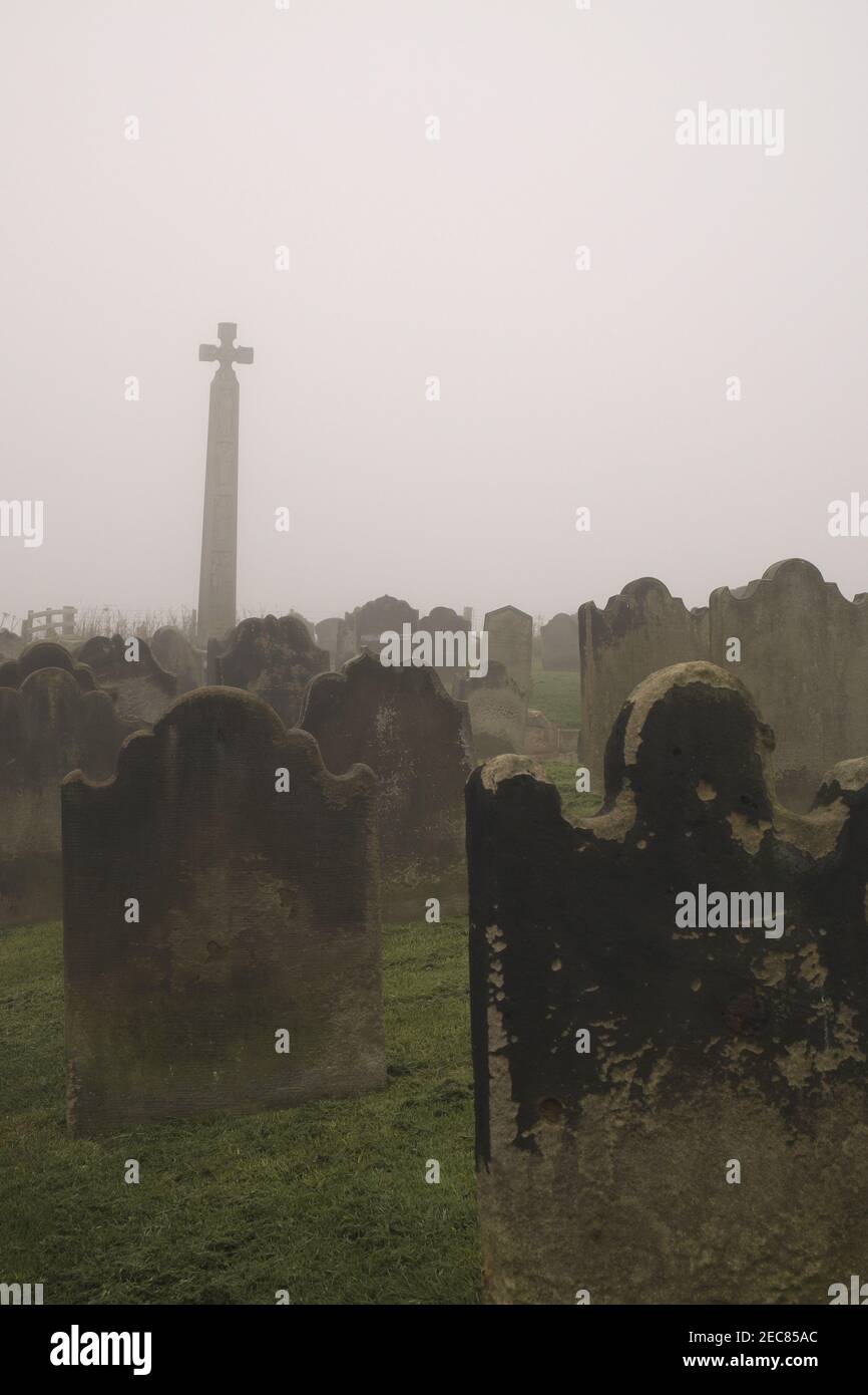 The Caedmon Cross and headstones on a misty day, St Mary's churchyard, Whitby, North Yorkshire, England, UK. Stock Photo