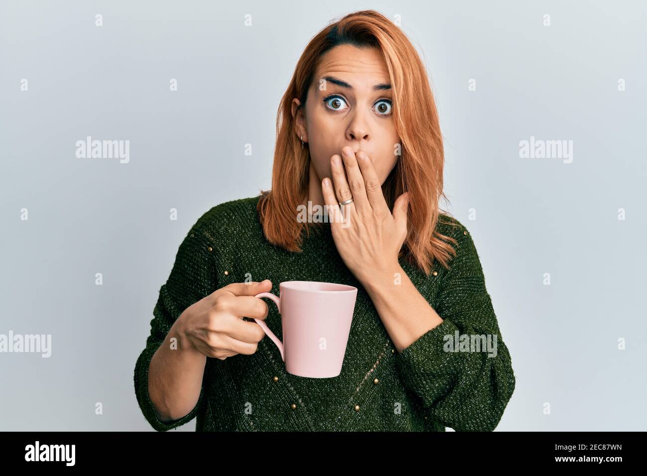 Hispanic young woman drinking a cup coffee covering mouth with hand
