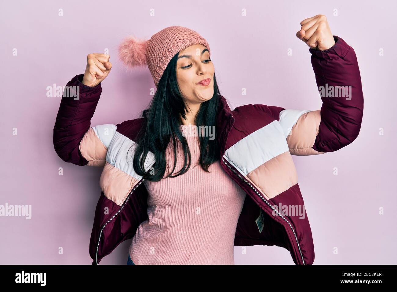 Young hispanic woman wearing wool winter sweater and cap showing arms muscles smiling proud. fitness concept. Stock Photo