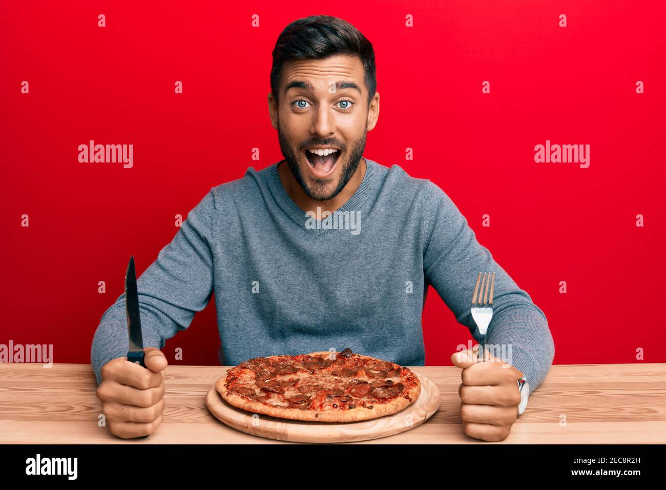 Handsome hispanic man eating tasty pepperoni pizza smiling and laughing