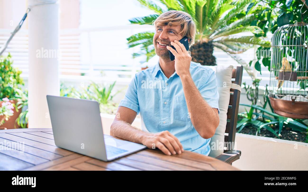 Middle age handsome man working at home using computer laptop and speaking on smartphone Stock Photo
