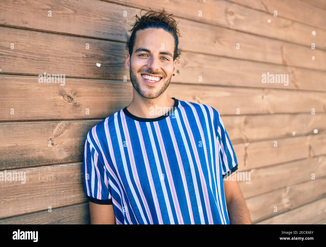 Young hispanic man smiling happy looking at the camera leaning on the ...