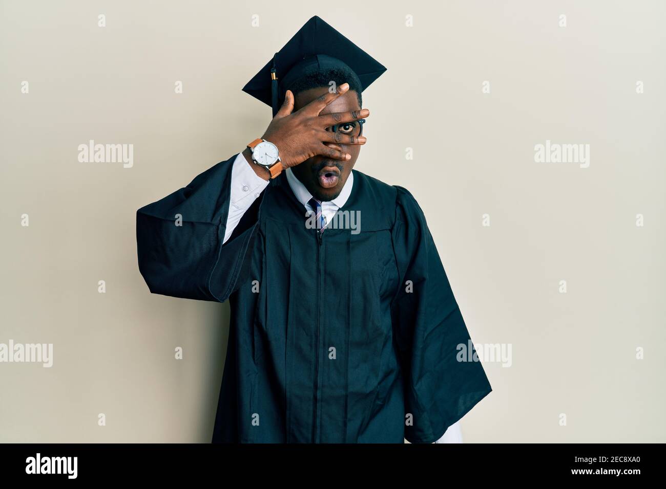 Handsome black man wearing graduation cap and ceremony robe peeking in ...