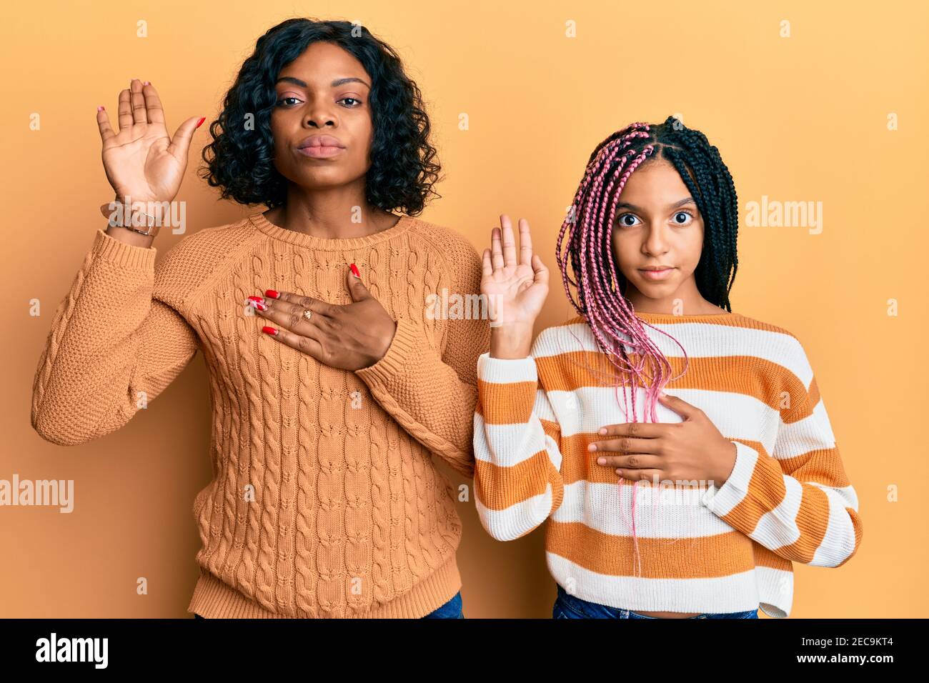 Beautiful african american mother and daughter wearing wool winter sweater  swearing with hand on chest and open palm, making a loyalty promise oath  Stock Photo - Alamy