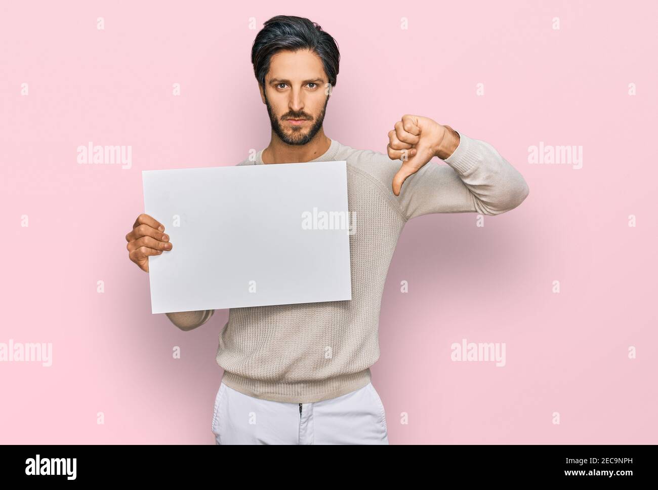 Young hispanic man holding blank empty banner with angry face, negative ...