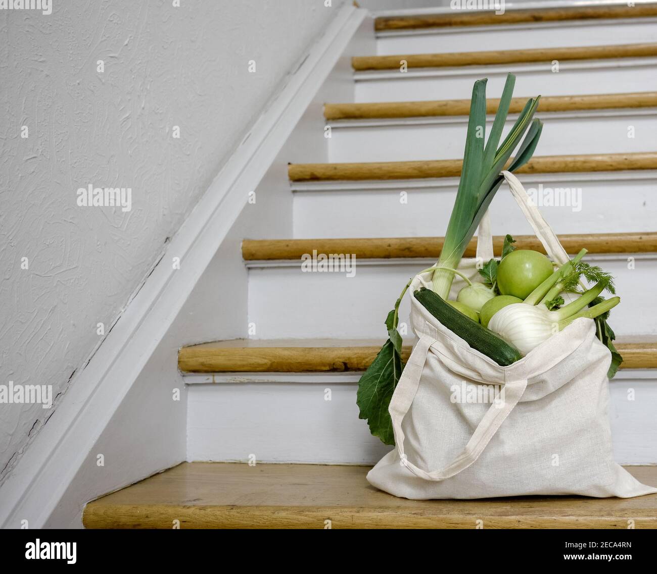 Sustainable reusable recycling cotton groceries bag with green vegetables and fruits from local organic market on the wooden staircase. Stock Photo