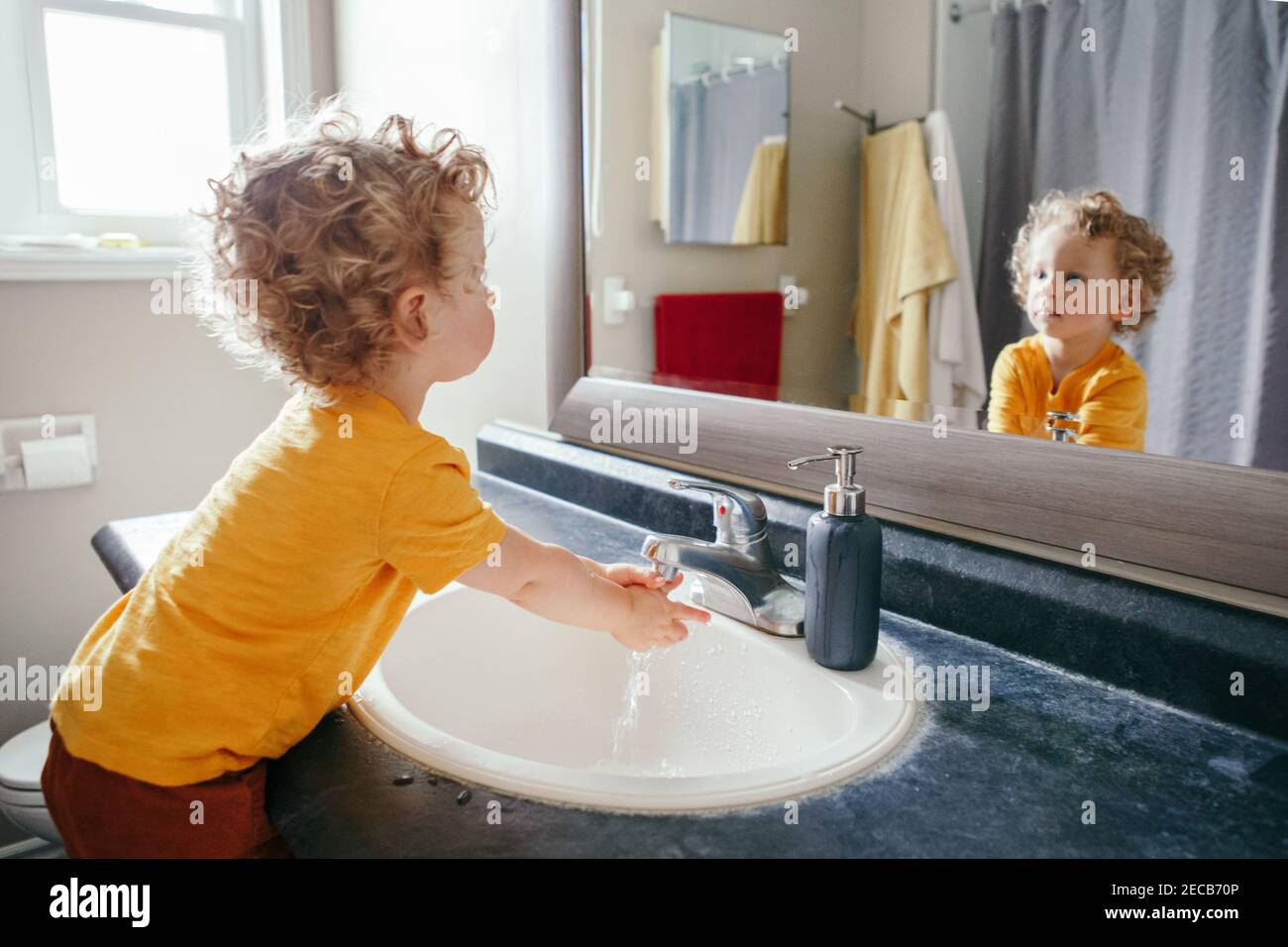 Little Caucasian boy toddler washing hands in bathroom at home. Health hygiene and morning routine for children. Cute funny child playing with water. Stock Photo