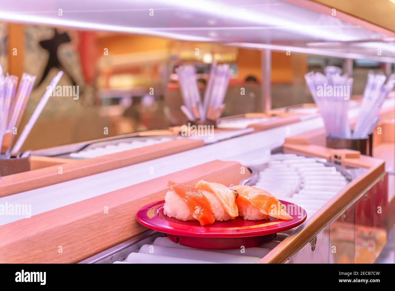 Close up on the roller of a conveyor belt sushi or Kaiten-zushi restaurant with a plate carrying three pieces of salmon sushi. Stock Photo