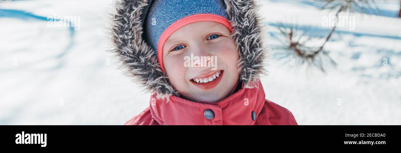 Cute adorable happy Caucasian smiling girl in pink jacket with fur hood during cold winter day. Kids outdoor seasonal activity. Funny face. Winter chi Stock Photo