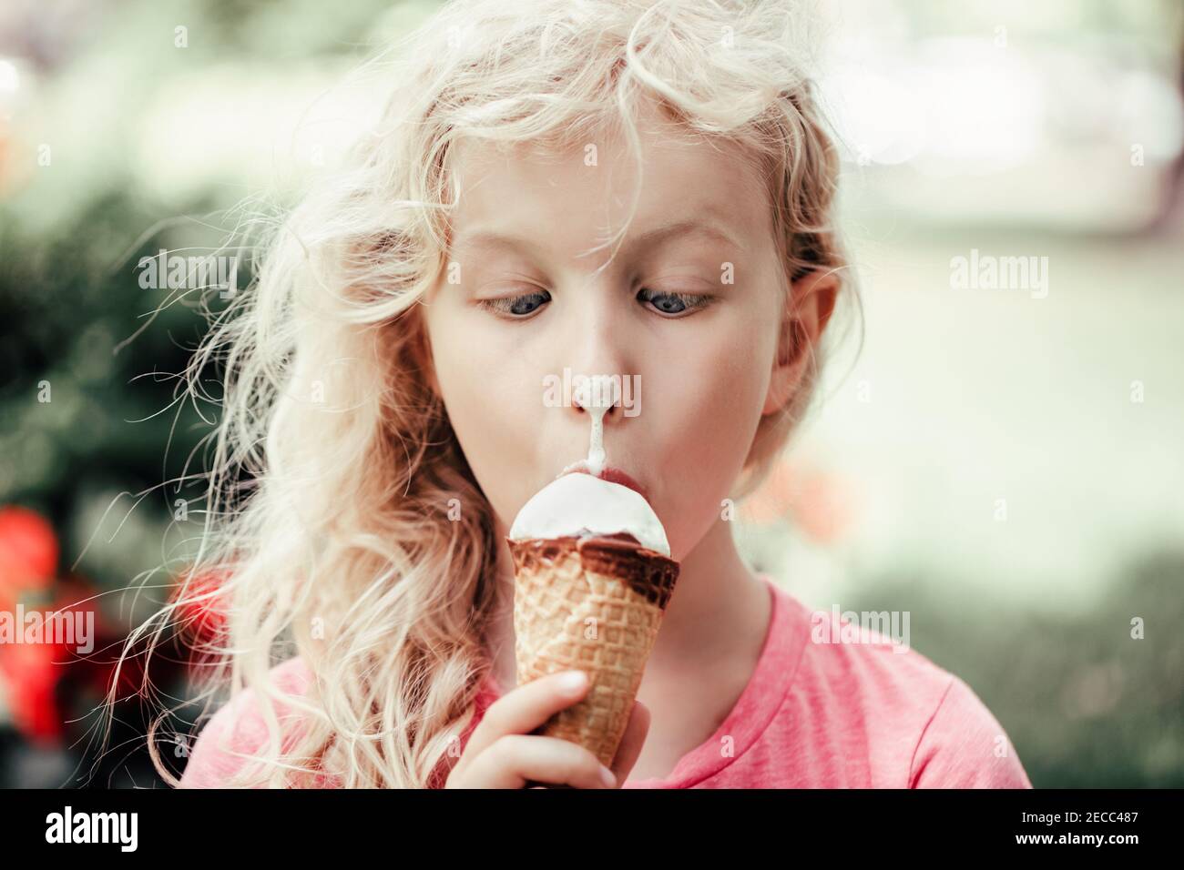 Cute funny adorable girl with dirty nose eating licking ice cream. Kid looking at food with crossed eyes. Hilarious child eating tasty sweet cold summ Stock Photo