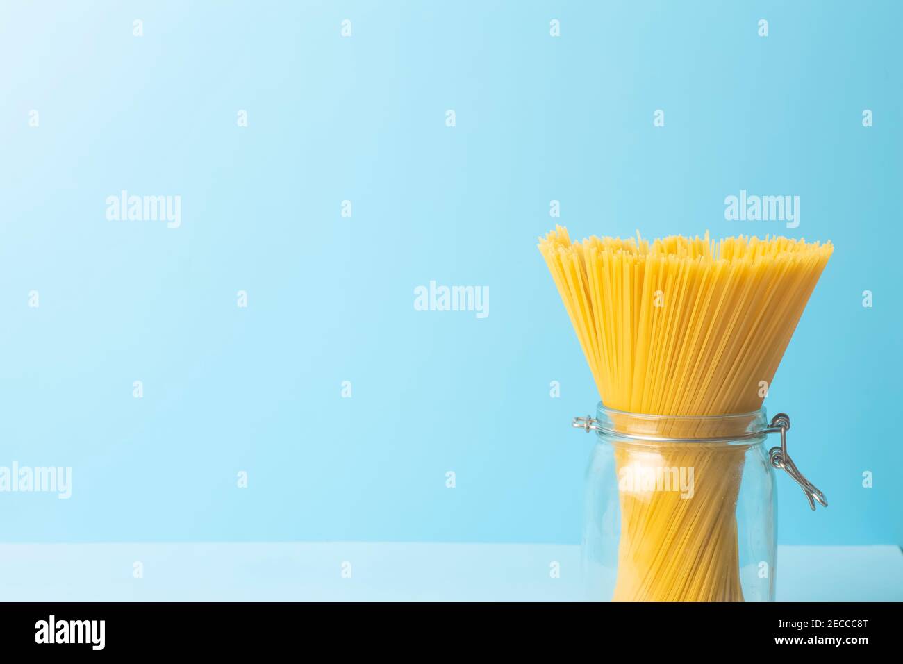 Spaghetti pasta on a blank blue background. Raw fresh isolated spaghetti in a jar before preparing italian food. Stock Photo