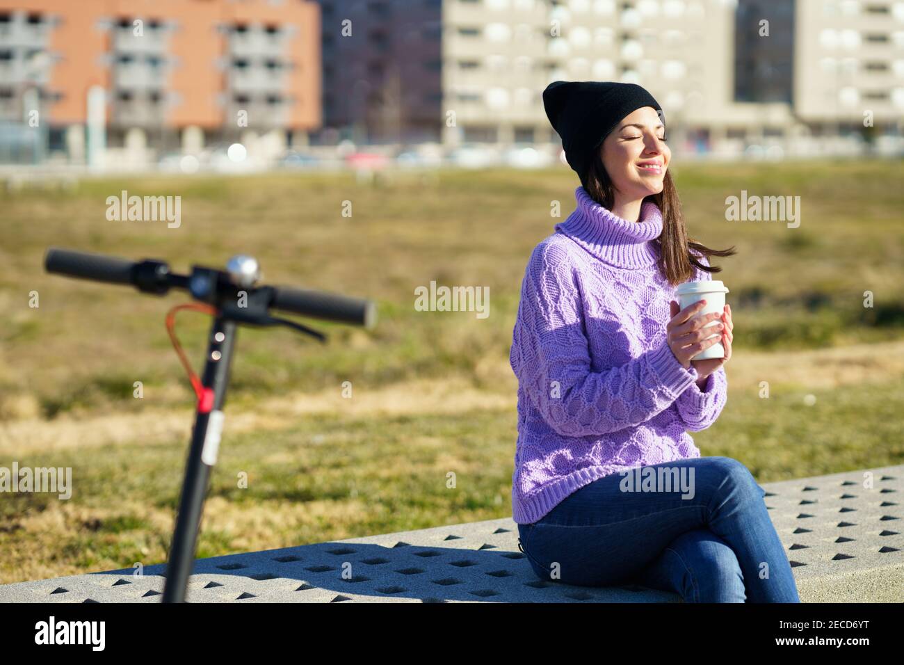 Female student with electric scooter enjoying the winter sunlight with her eyes closed. Stock Photo