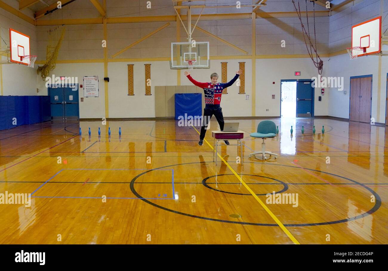A Physical Education teacher conducts a gym class in front of a laptop in an empty gymnasium for virtual students learning from home during the COVID- Stock Photo