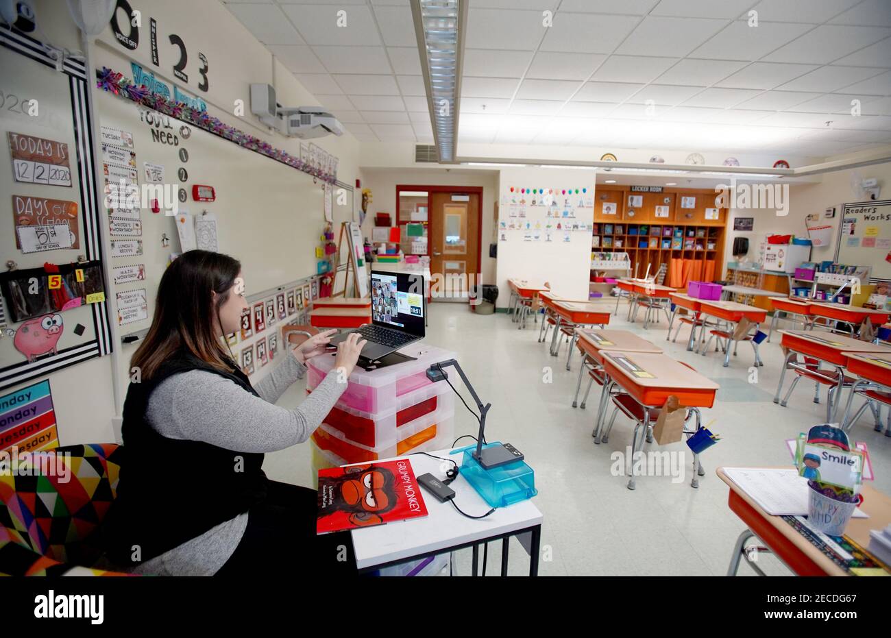A first grade teacher interacts with her students via Google Meet in an empty classroom while the students log in from home. Stock Photo