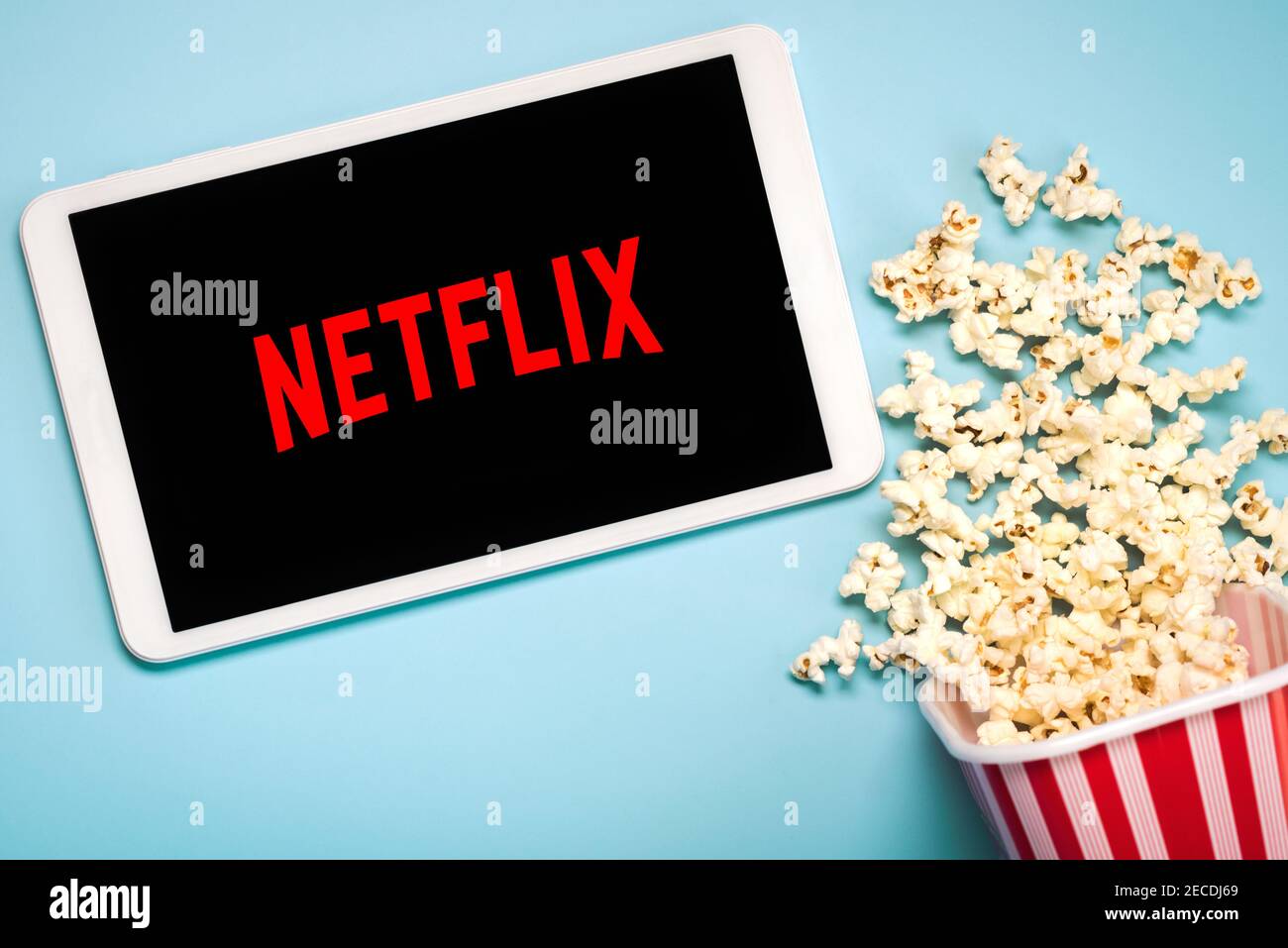 Netflix logo on the screen of a white digital tablet with popcorn on a blue background Stock Photo