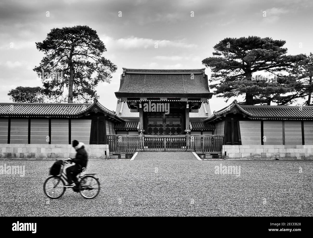 Colourless black white image of blurred lonely bicycle rider in front of historic gates to ancient imperial palace in Kyoto city of Japan. Stock Photo