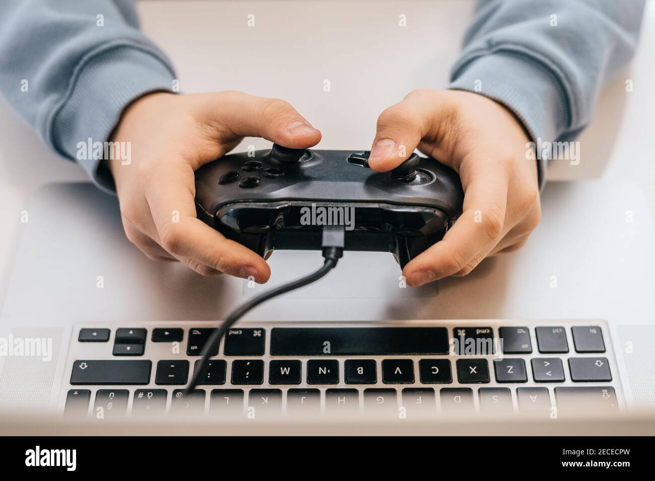 Close up view of young hands using a game pad with laptop to play games online. Details of videogames streamer playing at home console. Vlogger having Stock Photo