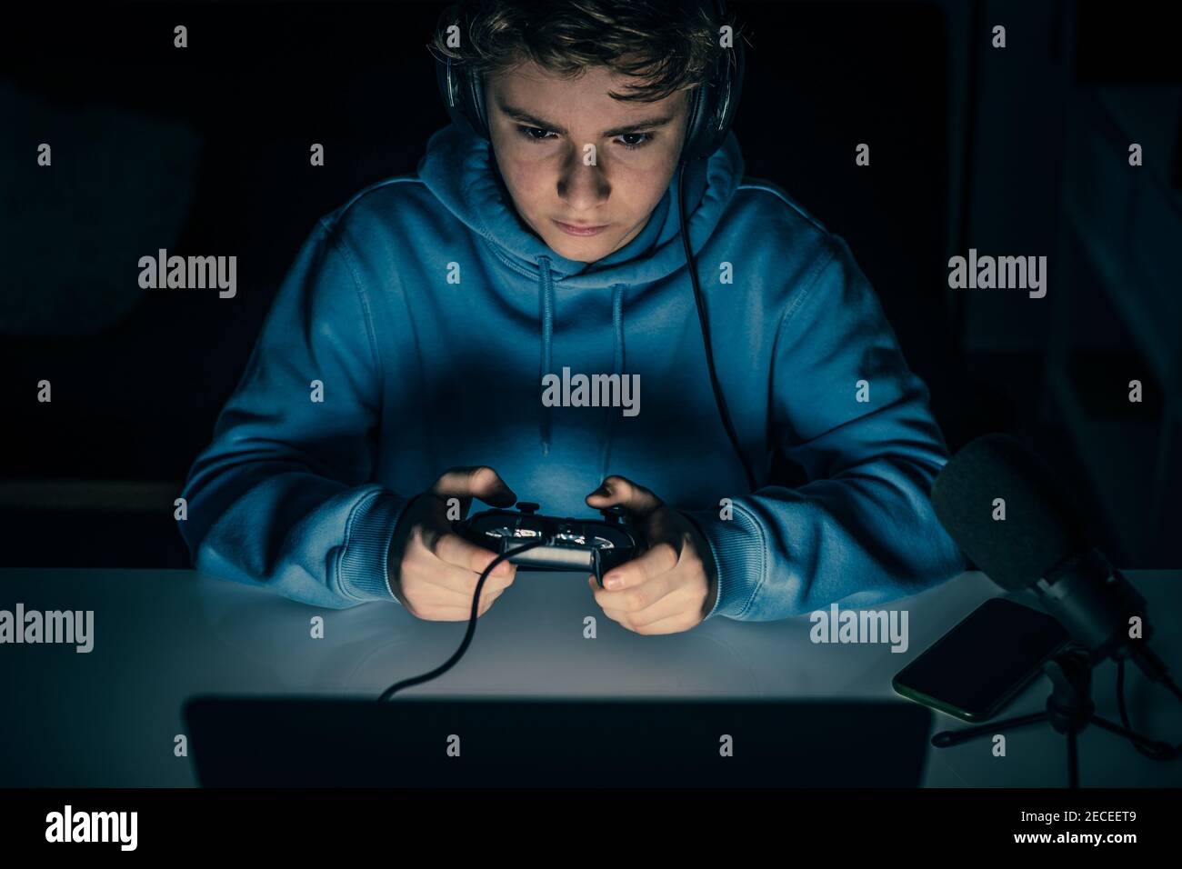 Young blogger and video game streamer playing at home with laptop. Vlogger filming himself having fun using technology to connect with audiences.Teena Stock Photo