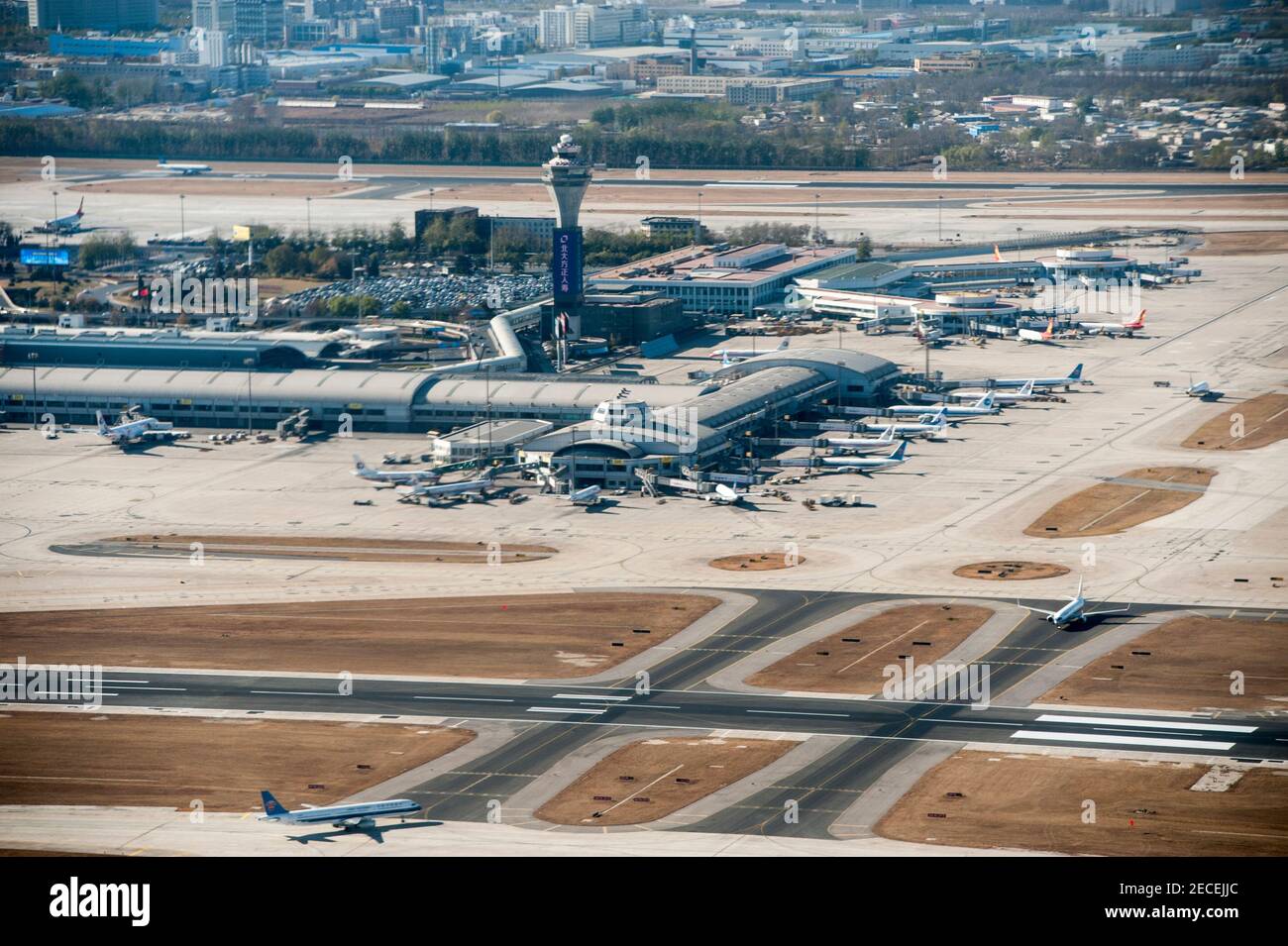 Aerial view of the runway, taxiways and various aircraft at the gates of Terminal 1 and Terminal 2 with its control tower on a sunny, blue sky, pollution-free day at Beijing Capital Airport, in the Shunyi district of the Chinese capital, Beijing, China, PRC. © Time-Snaps Stock Photo