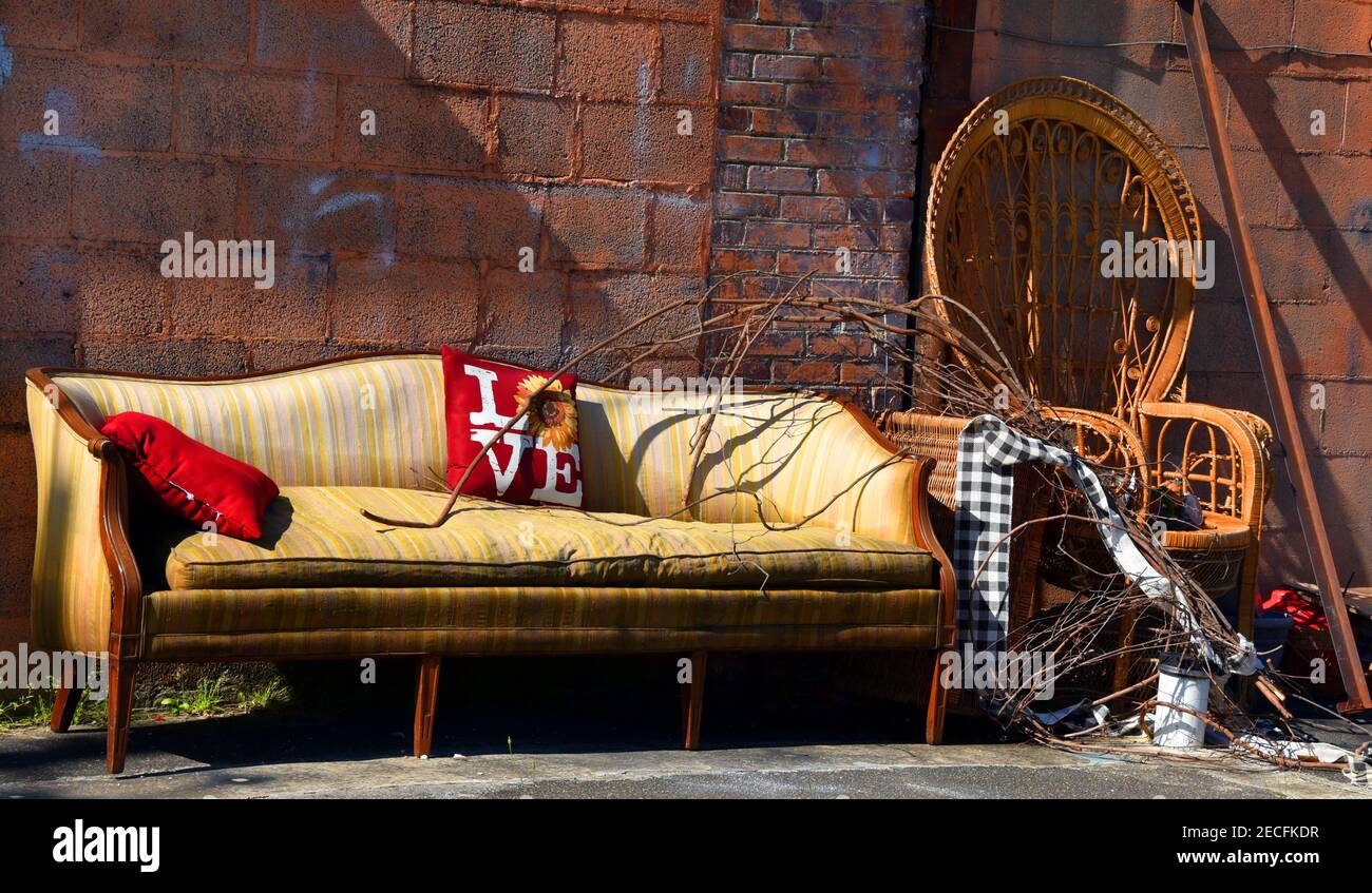 Outdoor living at its worst. Sofa and chair are wet and faded. They sit in  a pile of junk in an alley Stock Photo - Alamy