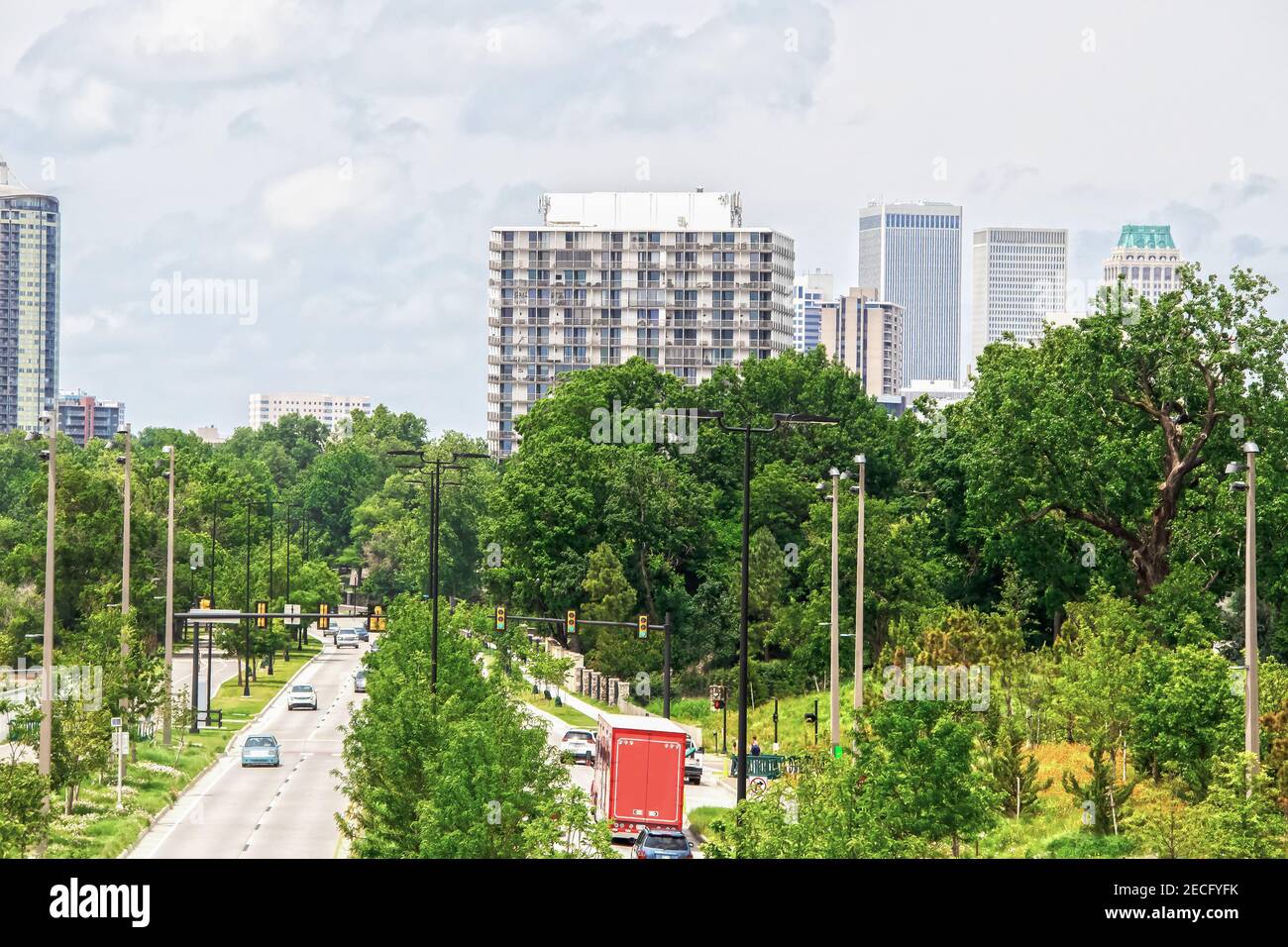 Divided highway with lots of lush foliage and green stoplight with cars and trucks and pedestrians leading to downtown Tulsa Oklahoma USA Stock Photo