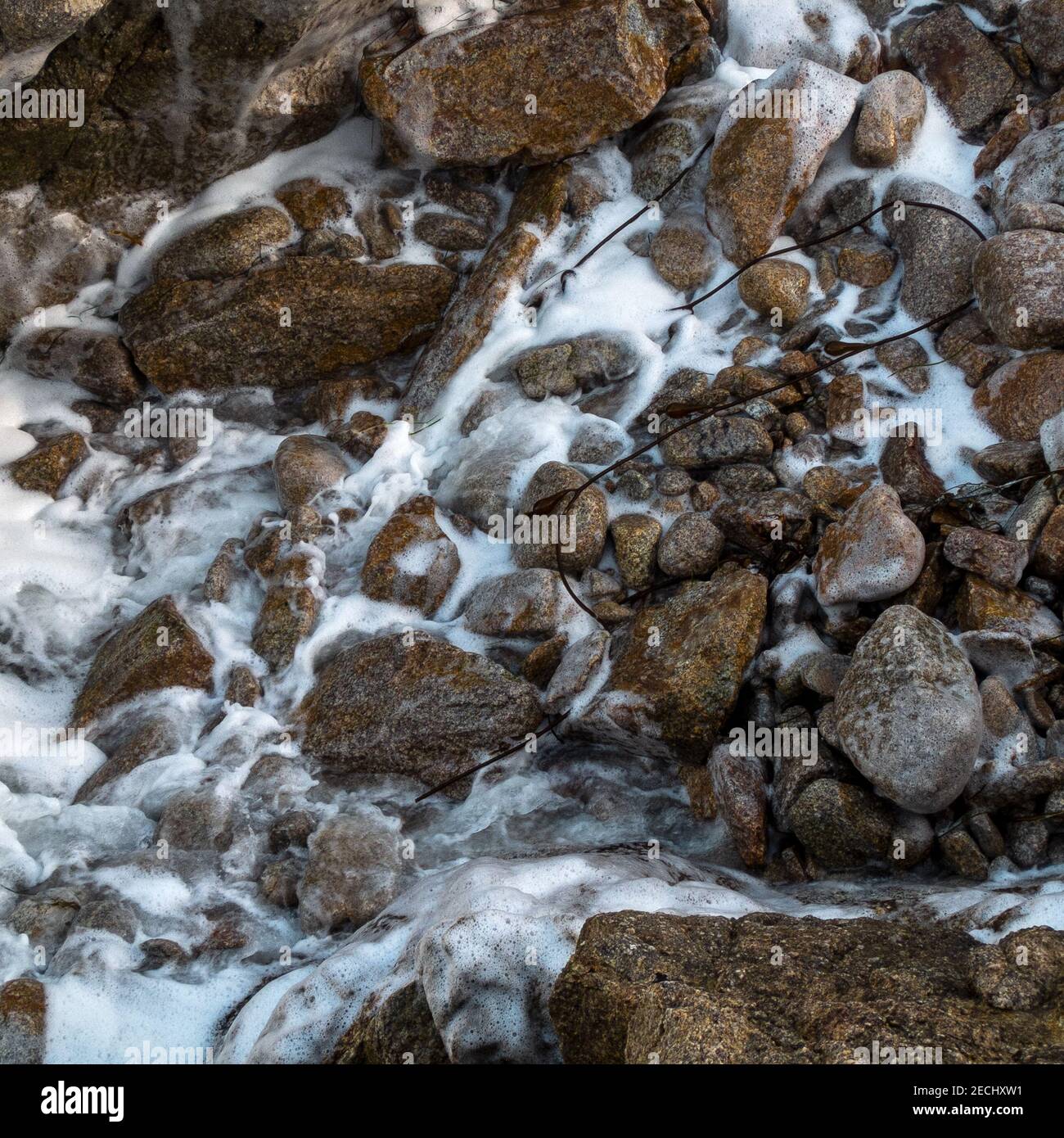Shoreline rocks and cobbles bathed in sea foam along the coast of California's Monterey Bay Stock Photo