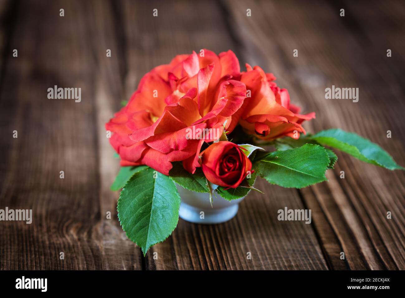 bouquet of small red roses in a vase on a wooden background Stock Photo