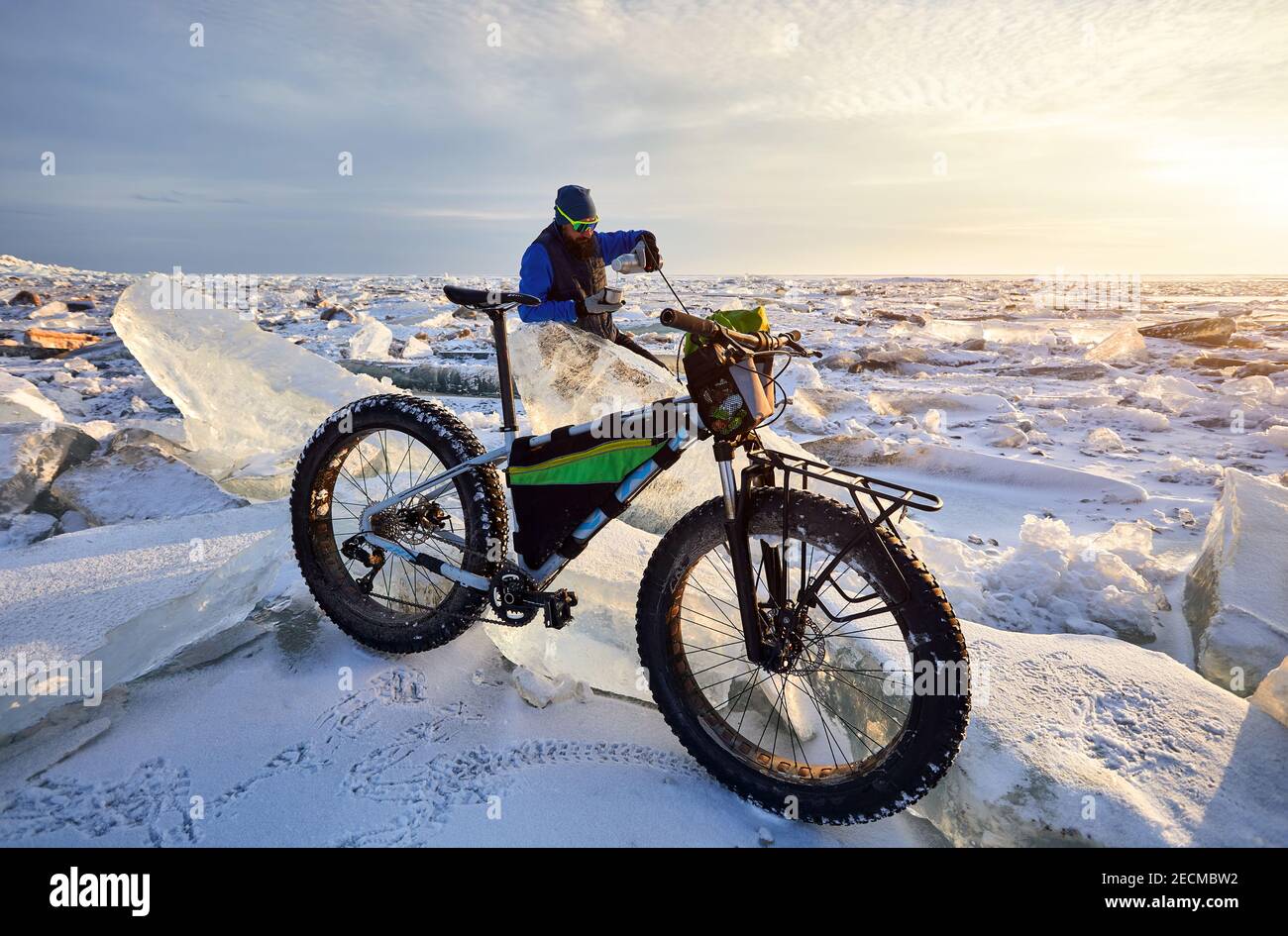 Man is have a tea brake near bicycle at frozen lake on sunset in Kazakhstan Stock Photo